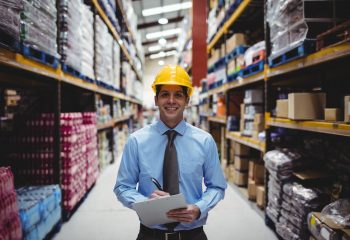 Smiling warehouse manager writing on clipboard in warehouse