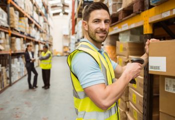 Warehouse worker scanning box while smiling at camera in a large warehouse