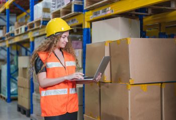 Female worker wear safety vest and yellow helmet with 
laptop checking goods stock in warehouse factory