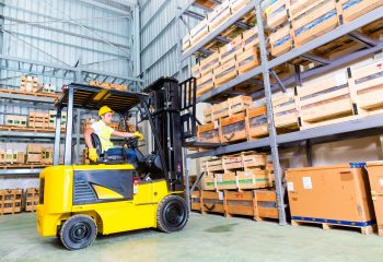 Asian fork lift truck driver lifting pallet in storage warehouse