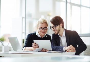 Contemporary employees with digital tablet watching video conference or online seminar while sitting in office