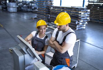 Industrial employees with yellow hardhat operating machines at production line using new software computer.