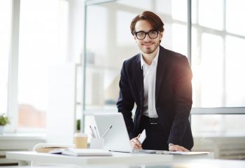 Young manager in formalwear leaning over workplace while standing up or sitting down