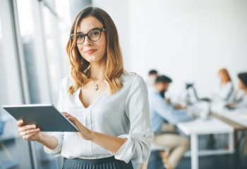 Young attractive female manager working on digital tablet while standing in modern office